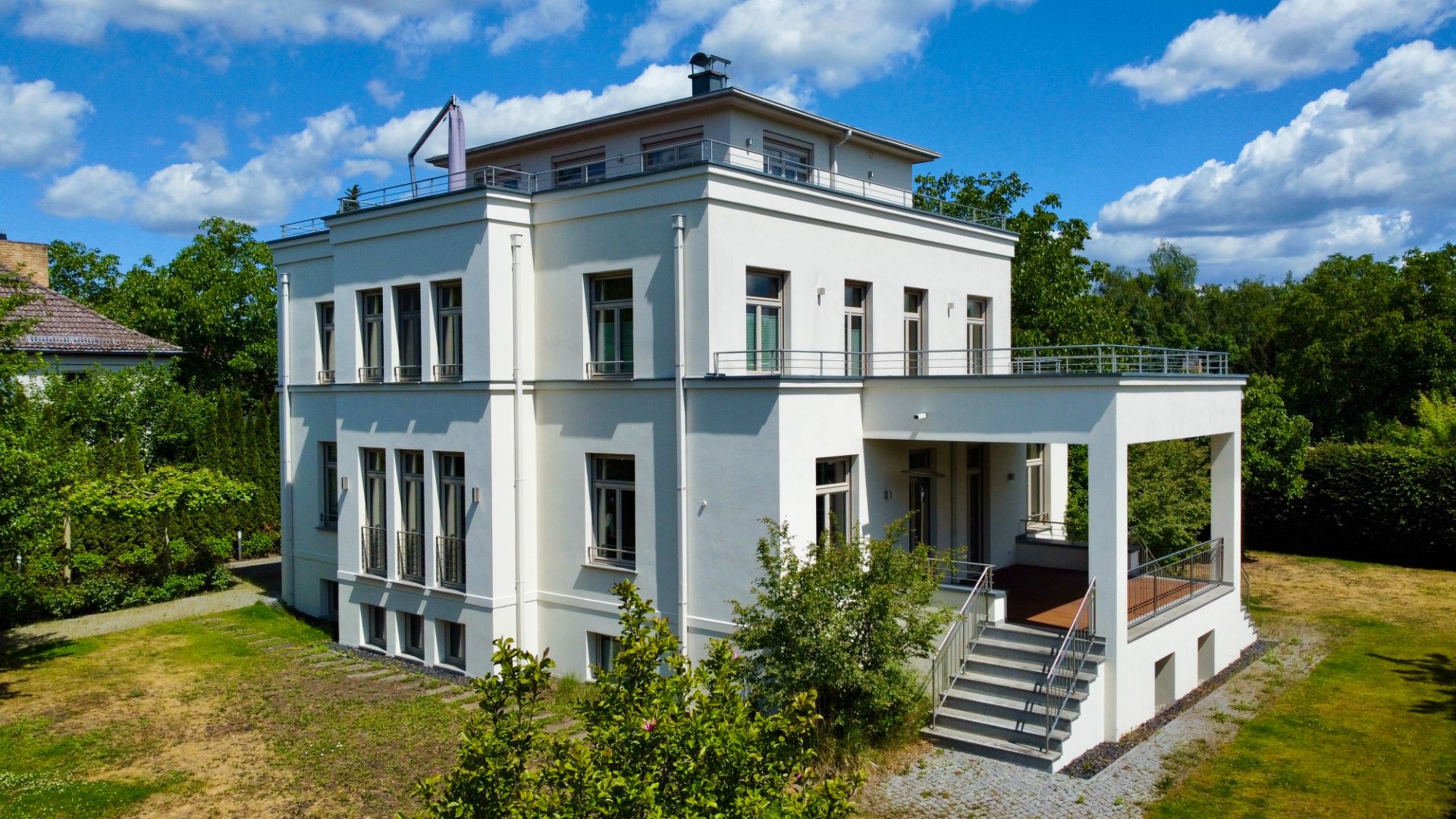 Zweistöckiges weißes Wohnhaus mit großem Balkon und Treppe im Garten.
