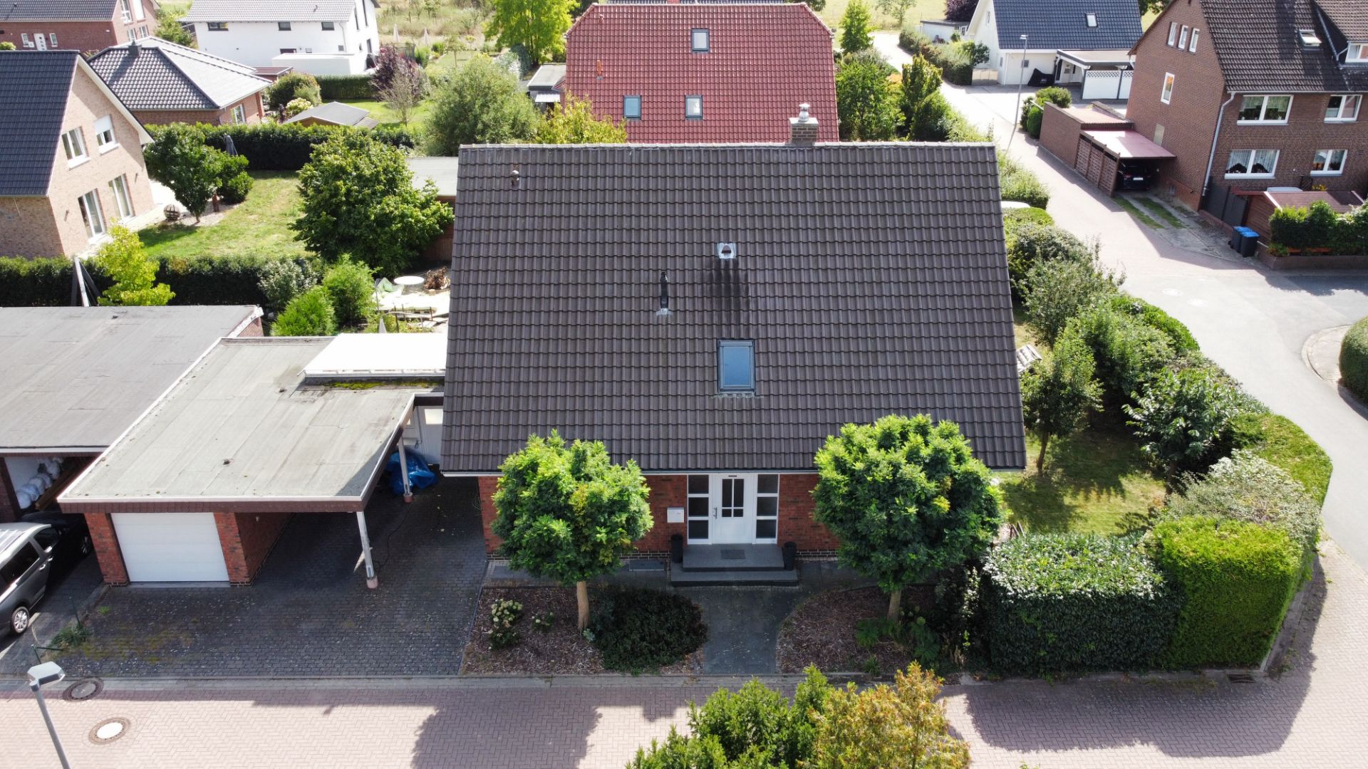 Ein Einfamilienhaus mit Satteldach, Vorgarten und angebautem Carport, von oben fotografiert.