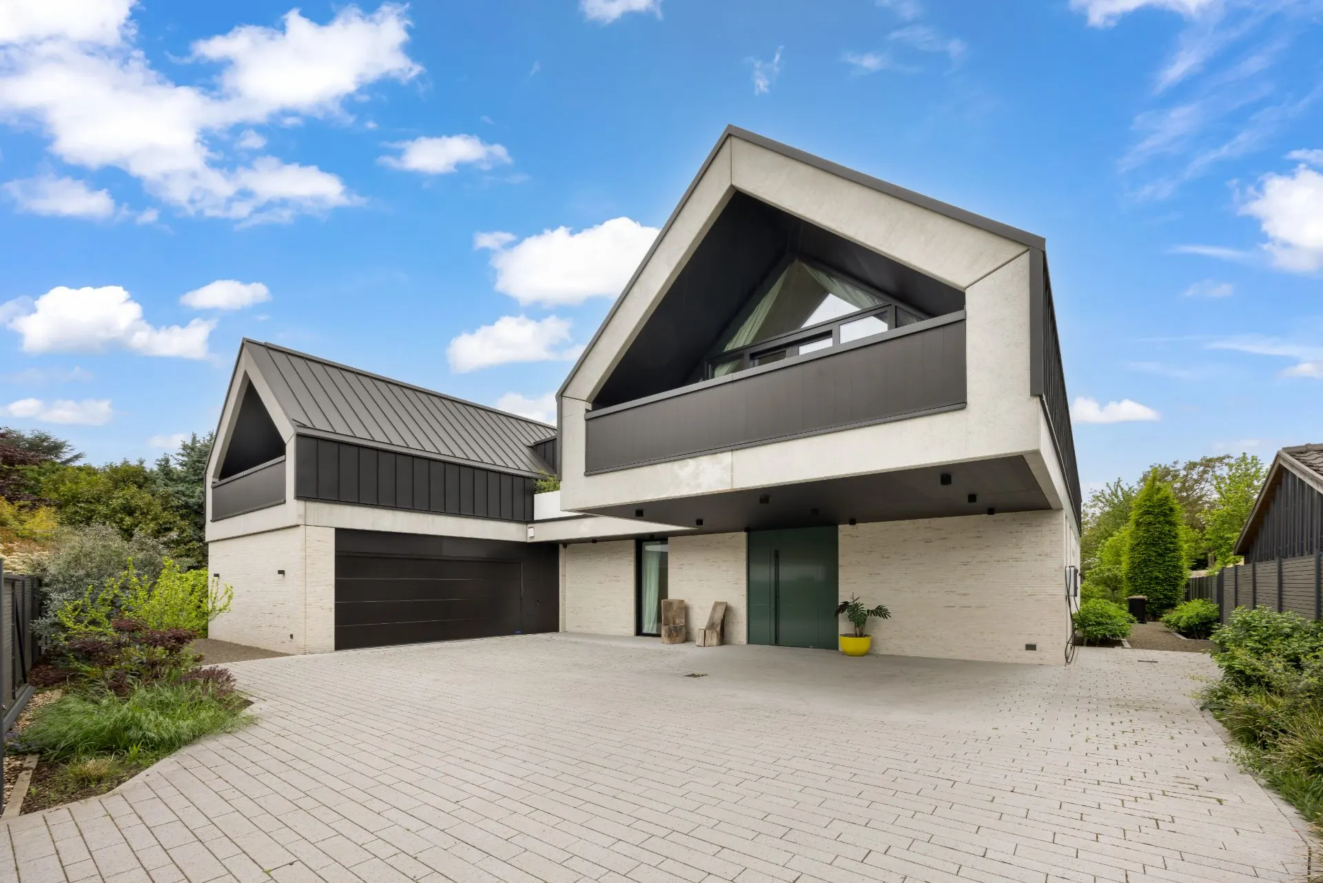 Modernes Wohnhaus mit zwei Giebeln, großer Einfahrt und Garage, umgeben von Pflanzen.