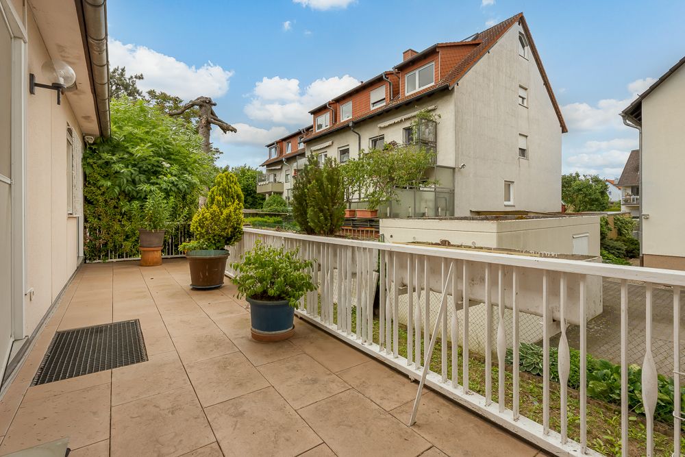 Geräumige Terrasse mit Geländer, mehreren Pflanzen in Töpfen und Blick auf benachbarte Wohnhäuser.