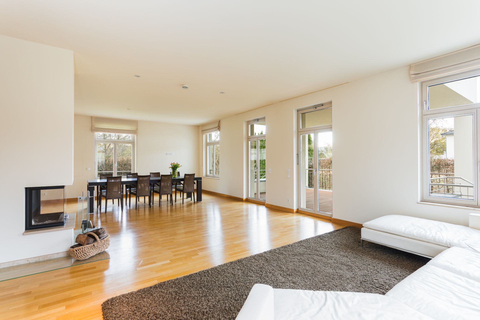 Helles Wohnzimmer mit Kamin, Esstisch, Stühlen, Sofa und großen Fenstern.