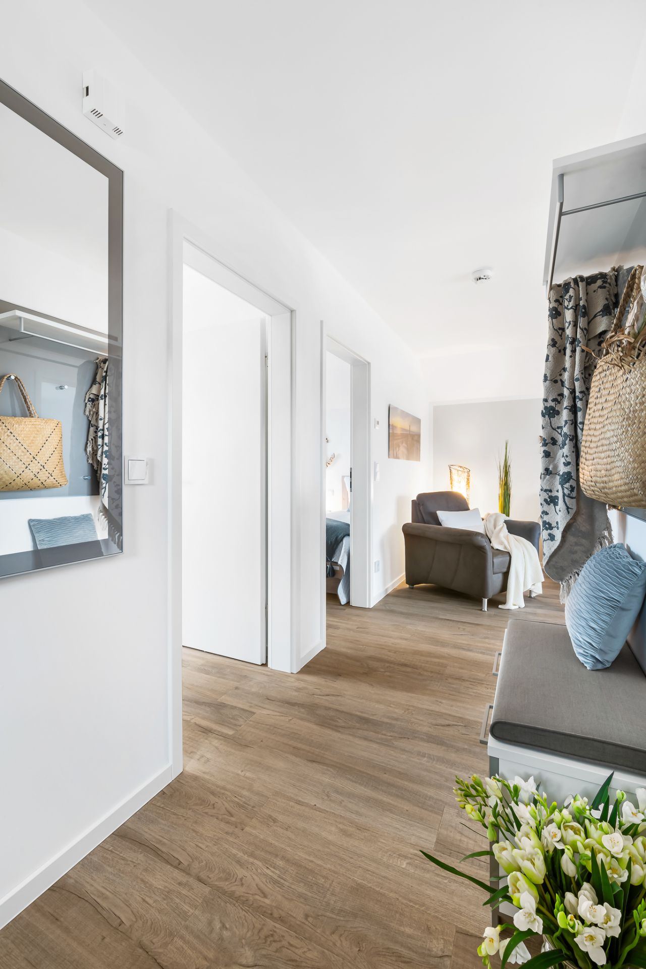 Heller Flur mit Holzfußboden, Spiegel, Sitzbank, Blumen und Blick ins Wohnzimmer.