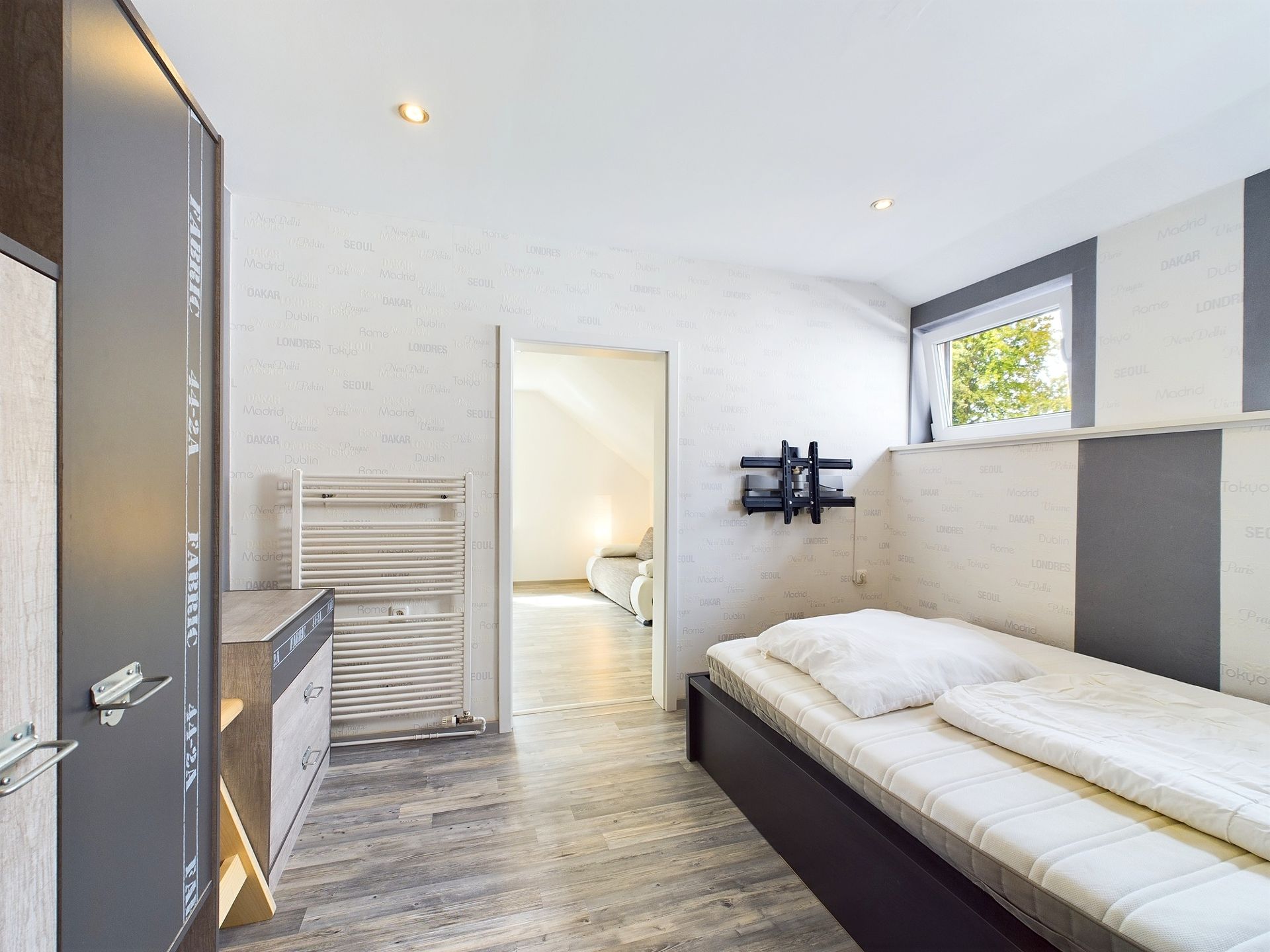 Modernes Schlafzimmer mit Einzelbett, Kleiderschrank und Fenster, Blick in ein weiteres Zimmer.