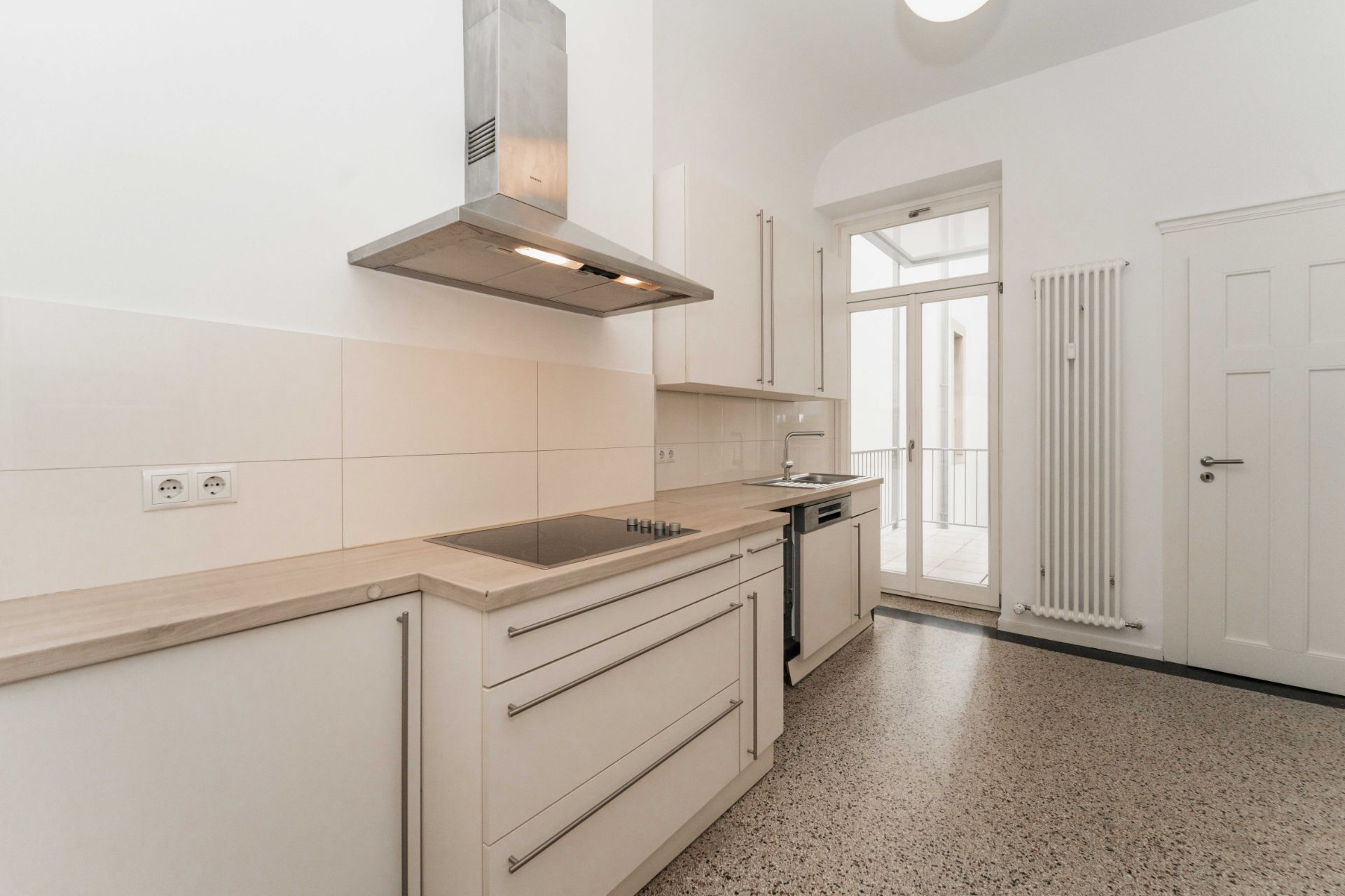 Moderne helle Einbauküche mit Herd, Backofen, Spüle und Tür zum Balkon.