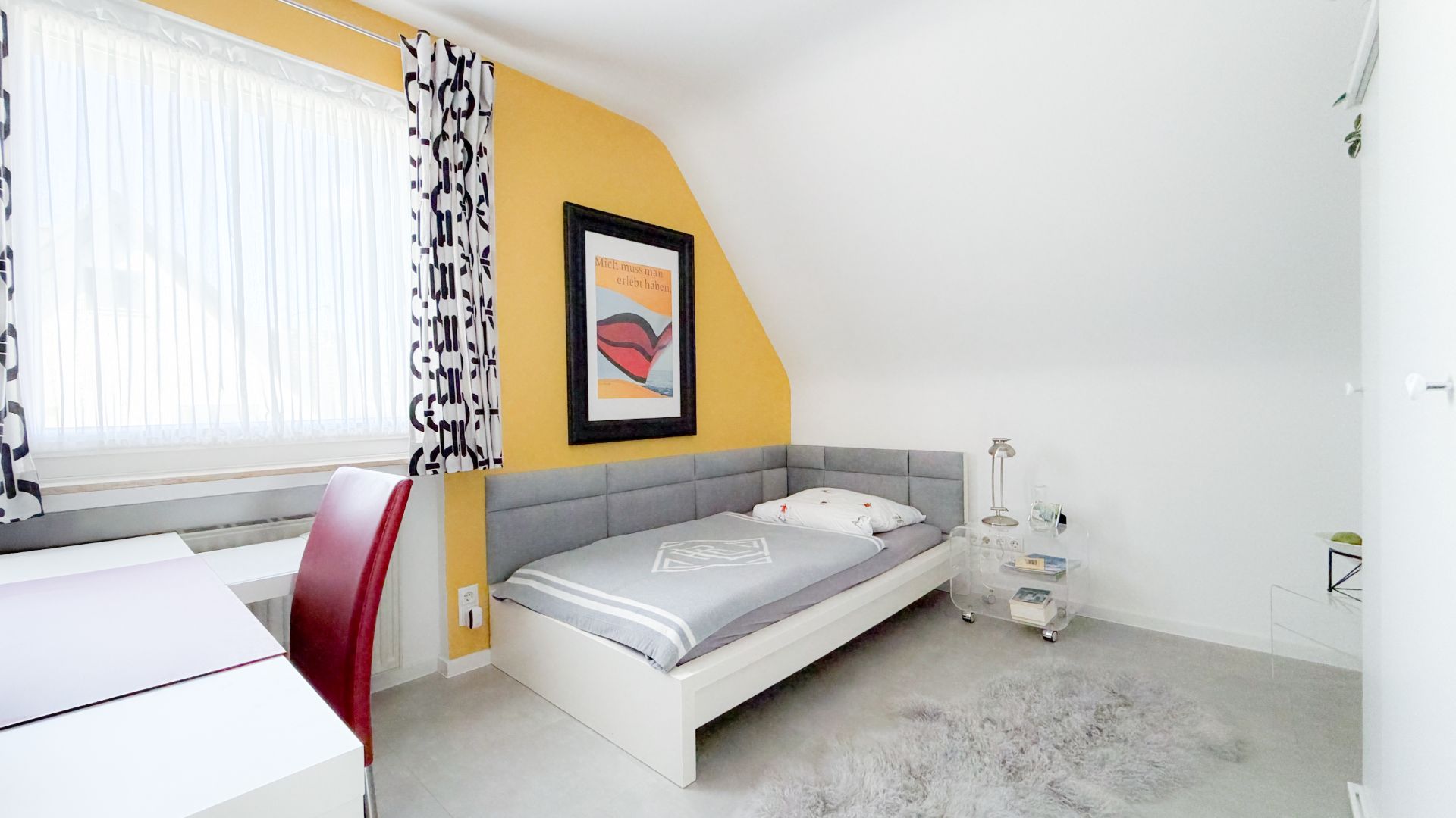 Helles Schlafzimmer mit Einzelbett, gelber Wand, Schreibtisch, Stuhl und Teppich.