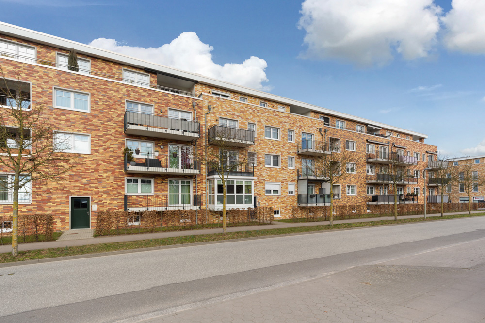Mehrstöckiges Wohngebäude mit Balkonen, Klinkerfassade und kleinen Bäumen vor dem Haus.