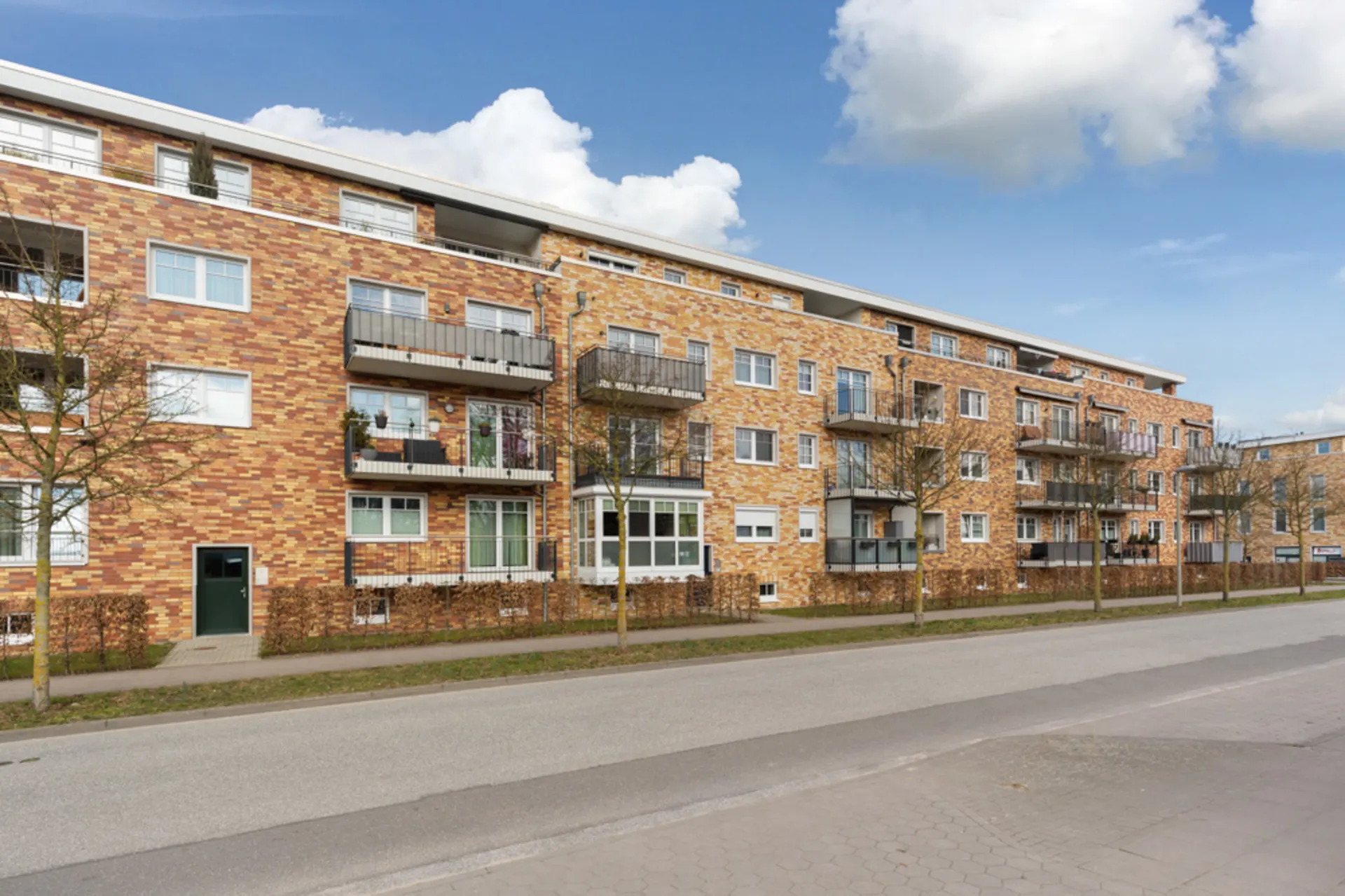 Mehrstöckiges Wohngebäude mit Balkonen, Klinkerfassade und kleinen Bäumen vor dem Haus.