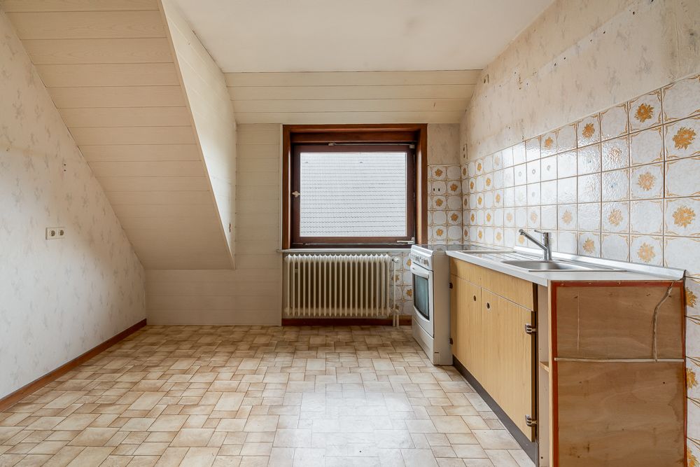 Leere Küche mit Fenster, Herd, Spüle und gemusterten Fliesen an der Wand.