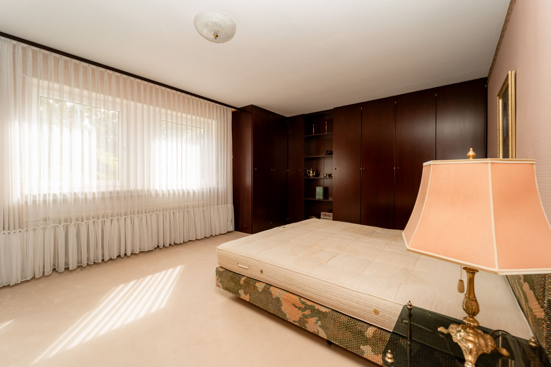 Helles Schlafzimmer mit großem Fenster, Bett und dunklem Einbauschrank.