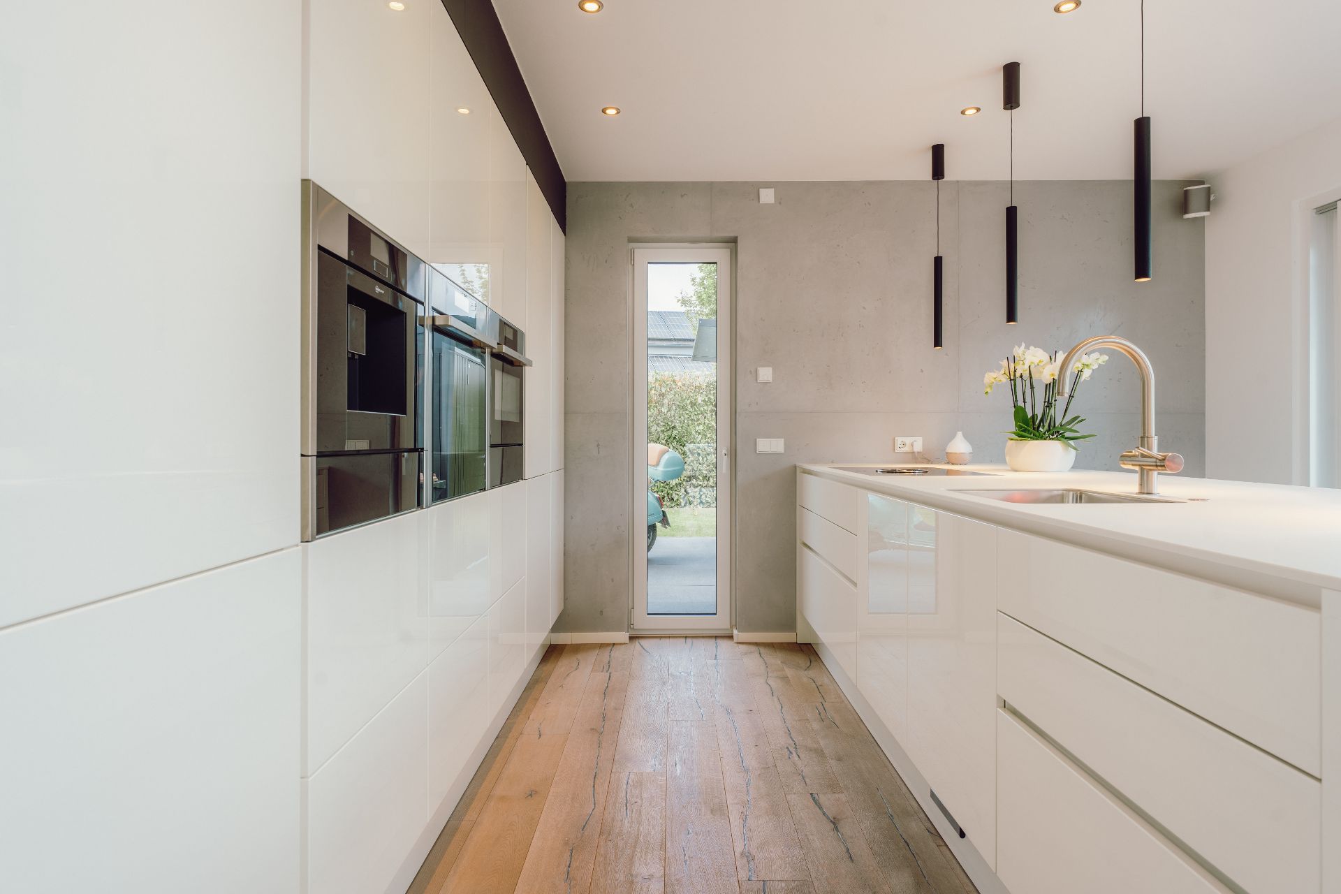 Moderne, helle Küche mit Holzboden, Kücheninsel, Hängelampen und Glastür zum Garten.