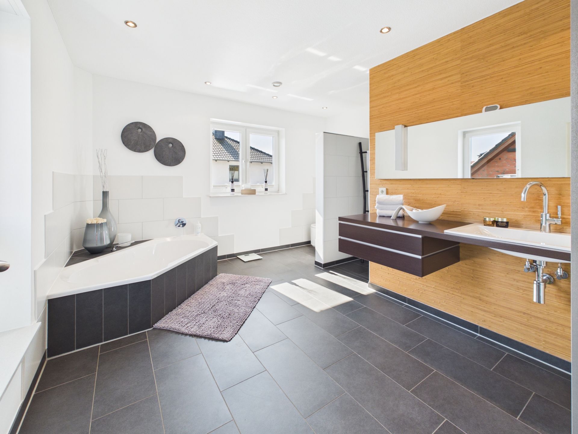 Modernes Badezimmer mit Eckbadewanne, Waschbecken, Spiegel und großem Fenster.