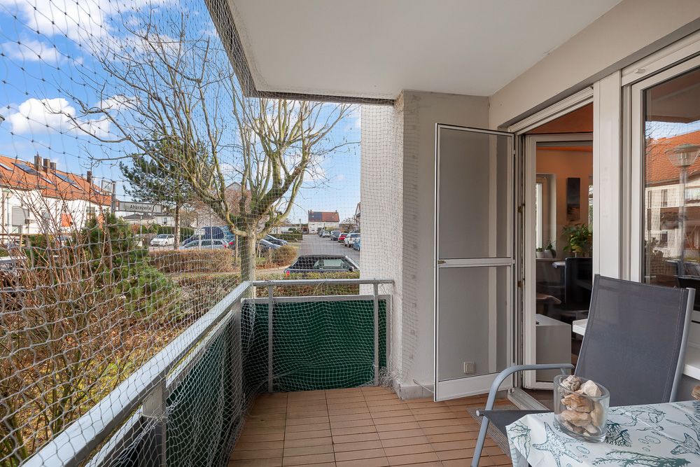 Überdachter Balkon mit Netz, Stuhl und kleinem Tisch, Blick auf Straße und Häuser.