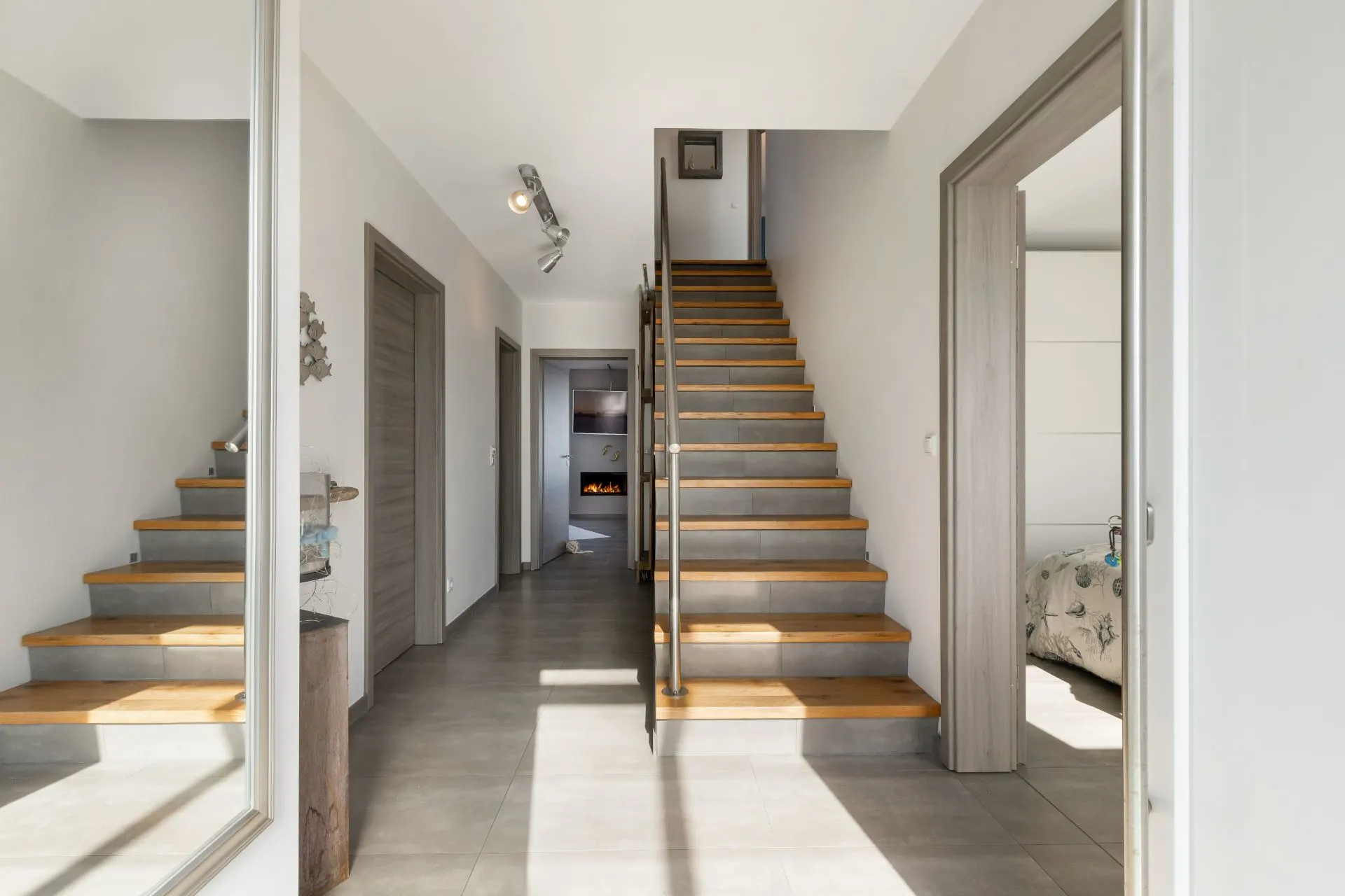 Heller Flur mit Treppe aus Holzstufen, grauem Boden und mehreren Türen zu angrenzenden Räumen.