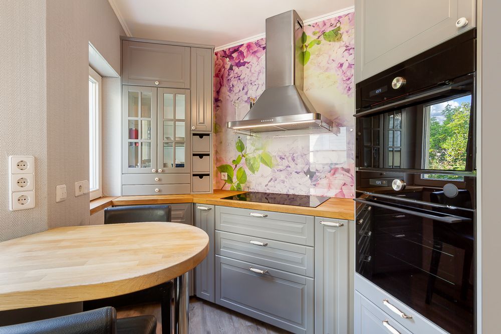 Moderne Küche mit grauen Schränken, Rundtisch und bunter Blumenrückwand hinter dem Herd.