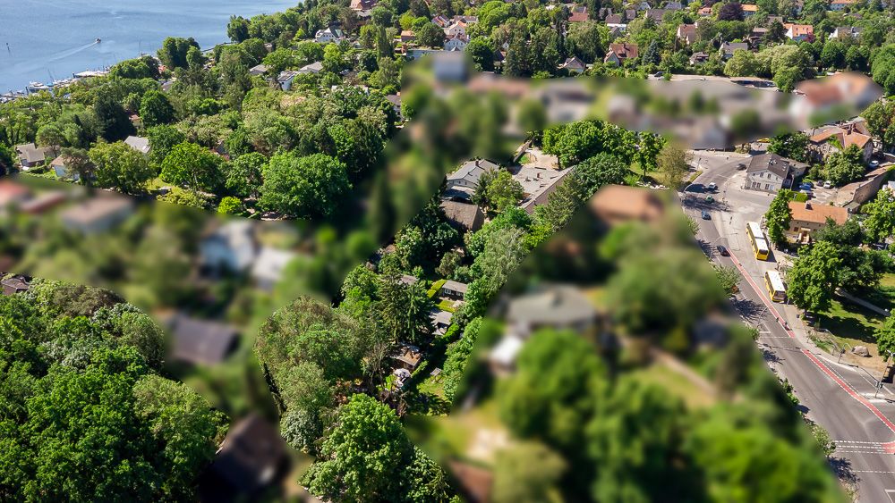 Luftaufnahme eines Wohngebiets mit vielen Bäumen, Straßen und einem See im Hintergrund.