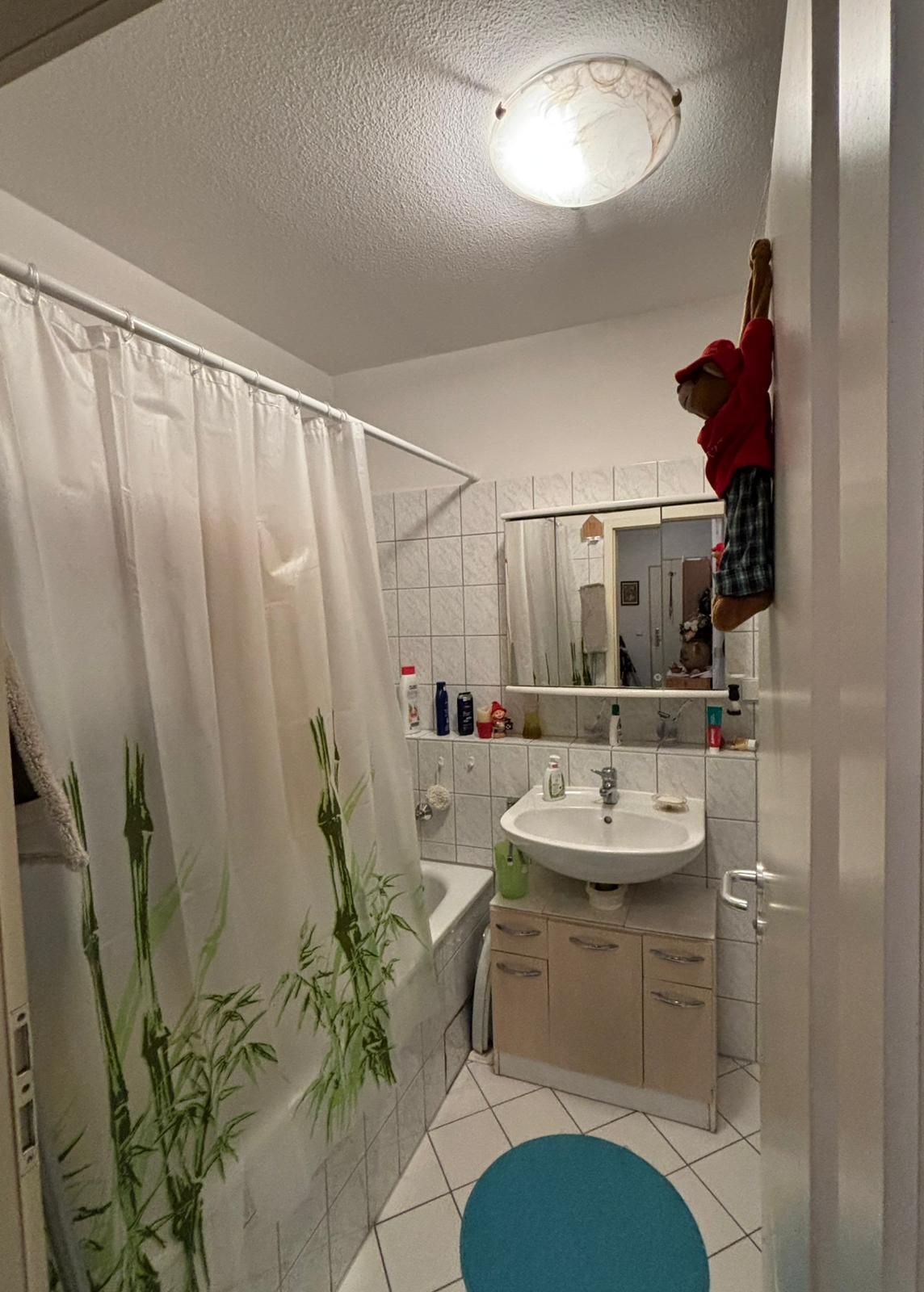Badezimmer mit Badewanne, Duschvorhang mit Bambusmotiv, Waschbecken, Spiegel und blauem Teppich.