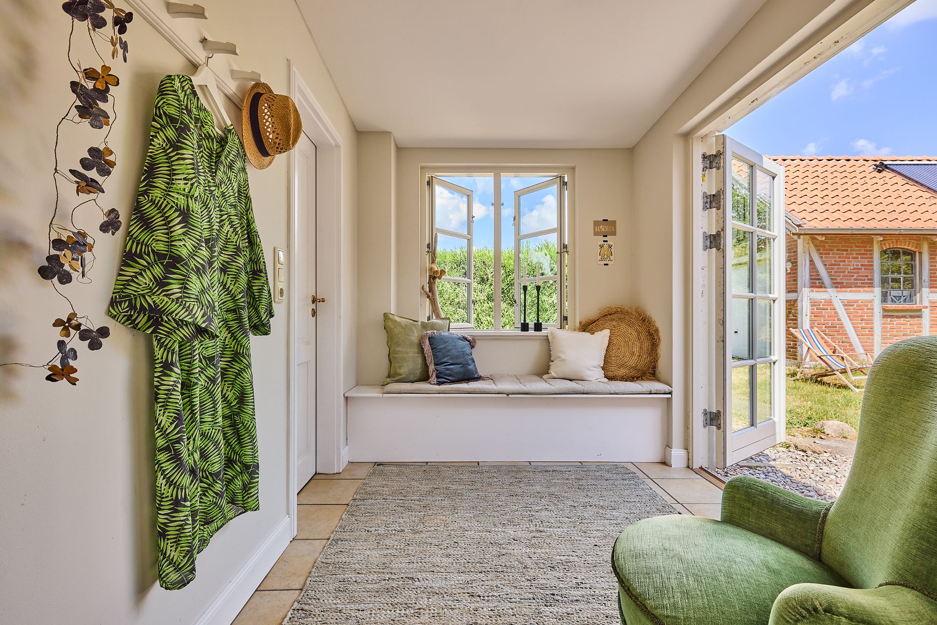 Heller Eingangsbereich mit Sitzbank am Fenster, grüner Sessel und offener Tür zum Garten.