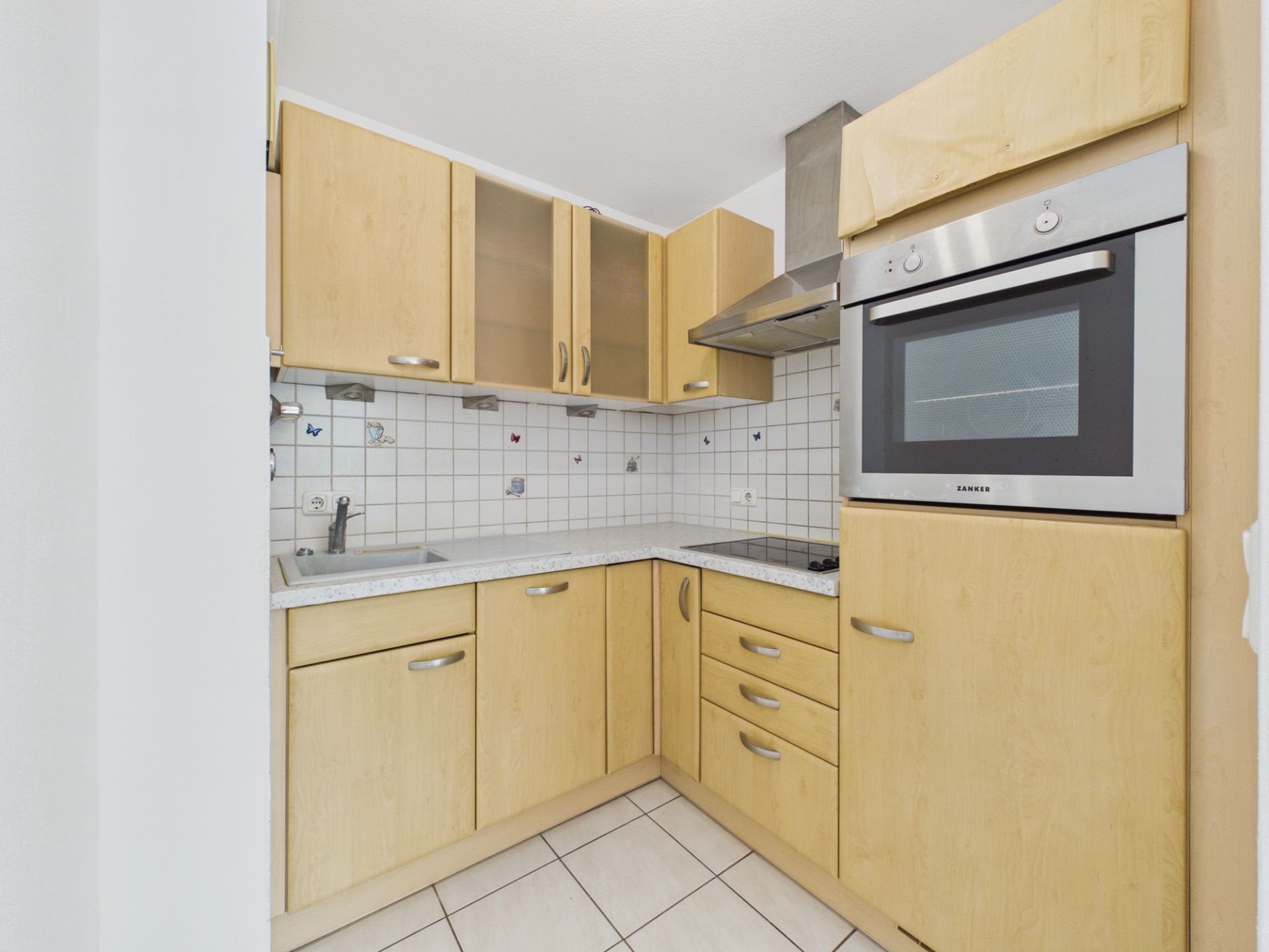 Kleine, helle Einbauküche mit Holzfronten, Herd, Backofen und Spüle.