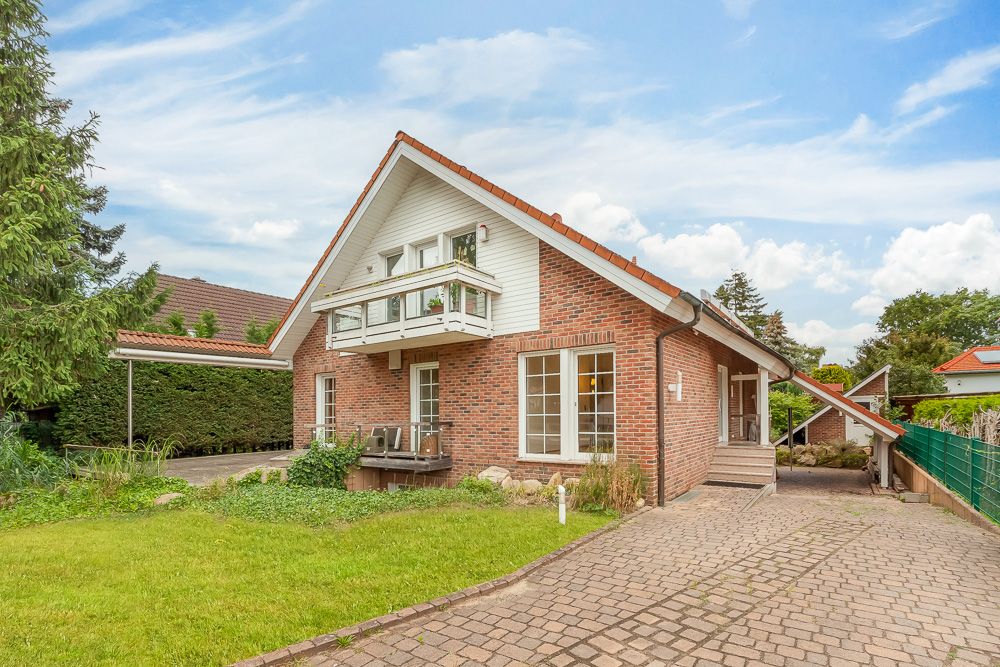 Backsteinhaus mit Satteldach, Balkon und großem Garten, gepflasterte Einfahrt im Vordergrund.