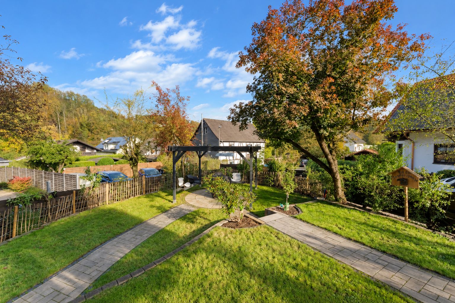 Gepflegter Garten mit Wegen, Rasen, Bäumen und einer Holzpergola in Wohngebiet.