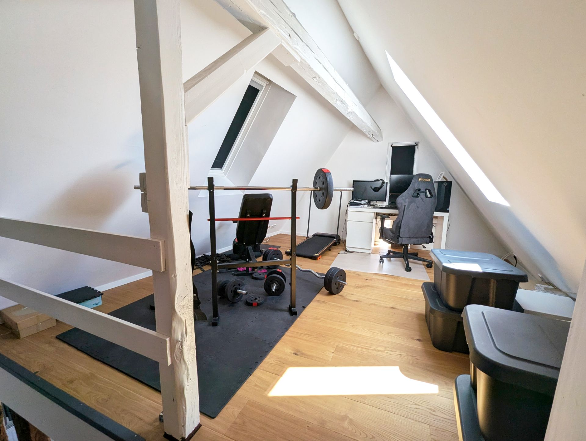 Dachzimmer mit Hantelbank, Computerarbeitsplatz und mehreren Aufbewahrungsboxen.