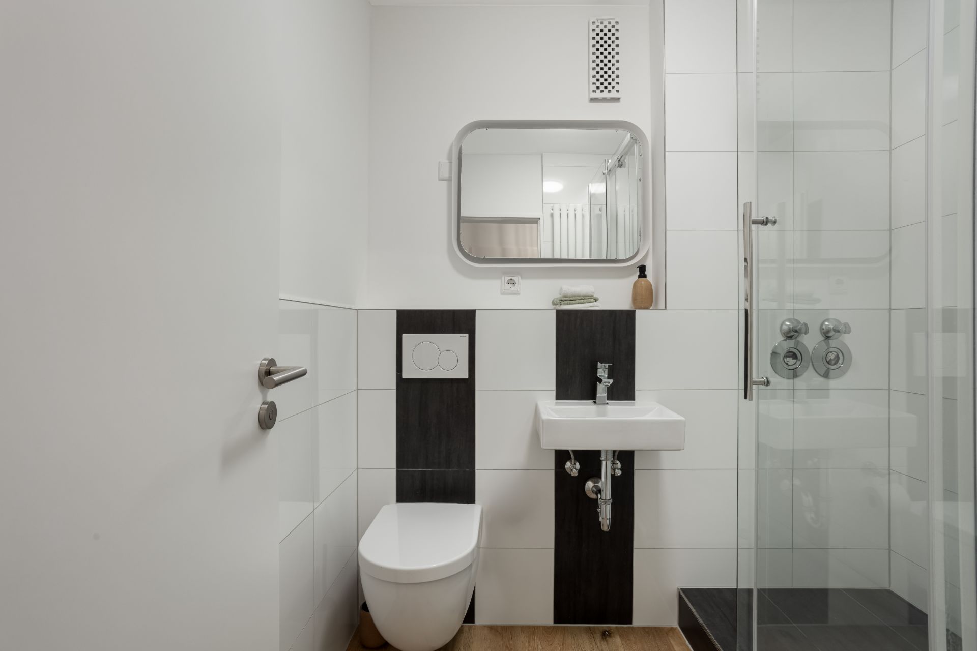 Modernes Badezimmer mit Toilette, Waschbecken, Spiegel und Glasduschkabine.