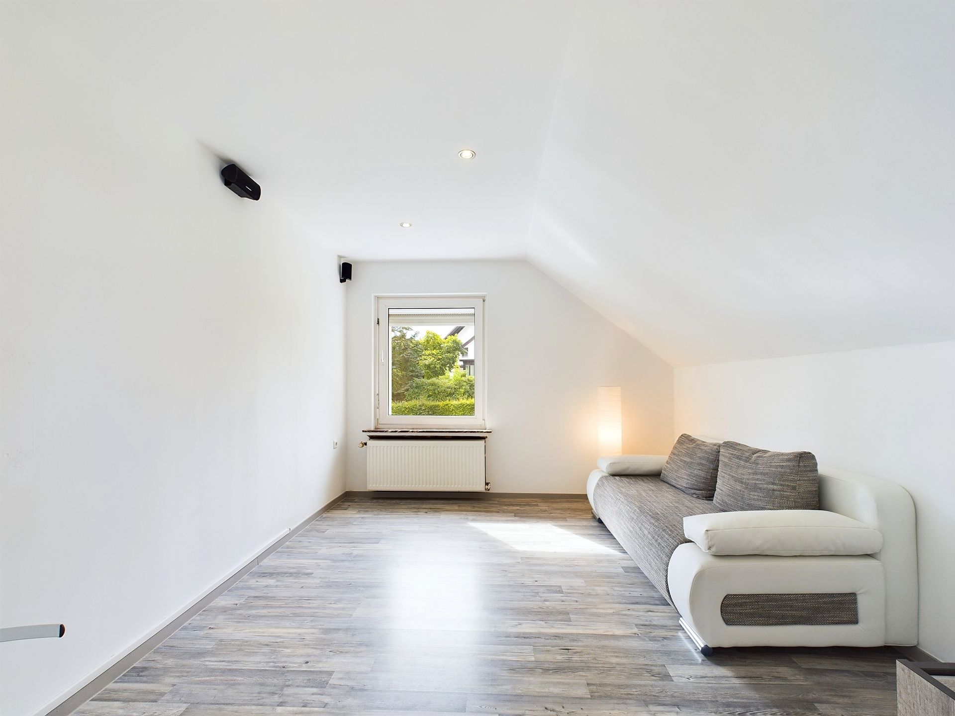 Helles Zimmer mit grauem Sofa, Fenster und Holzfußboden.