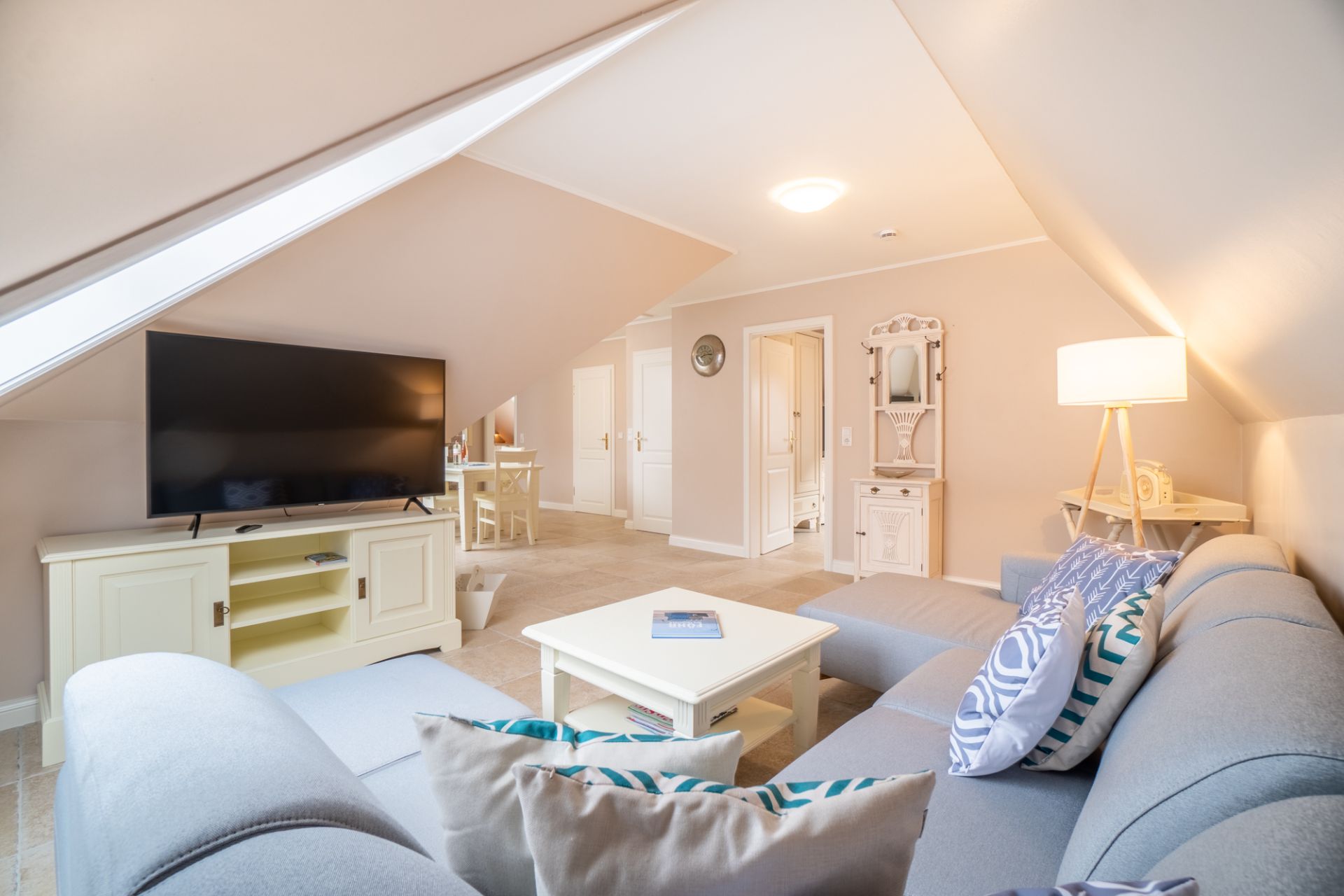 Helles Wohnzimmer mit großer Eckcouch, Fernseher, Couchtisch und Stehlampe unter Dachschrägen.