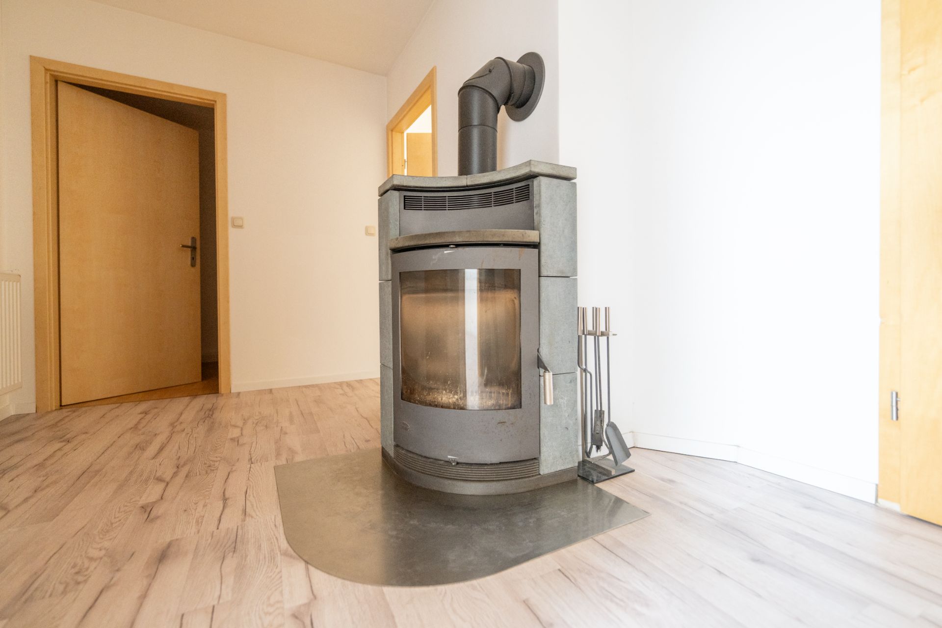 Freistehender Kaminofen auf Holzfußboden in einem hellen Flur mit offenen Holztüren.