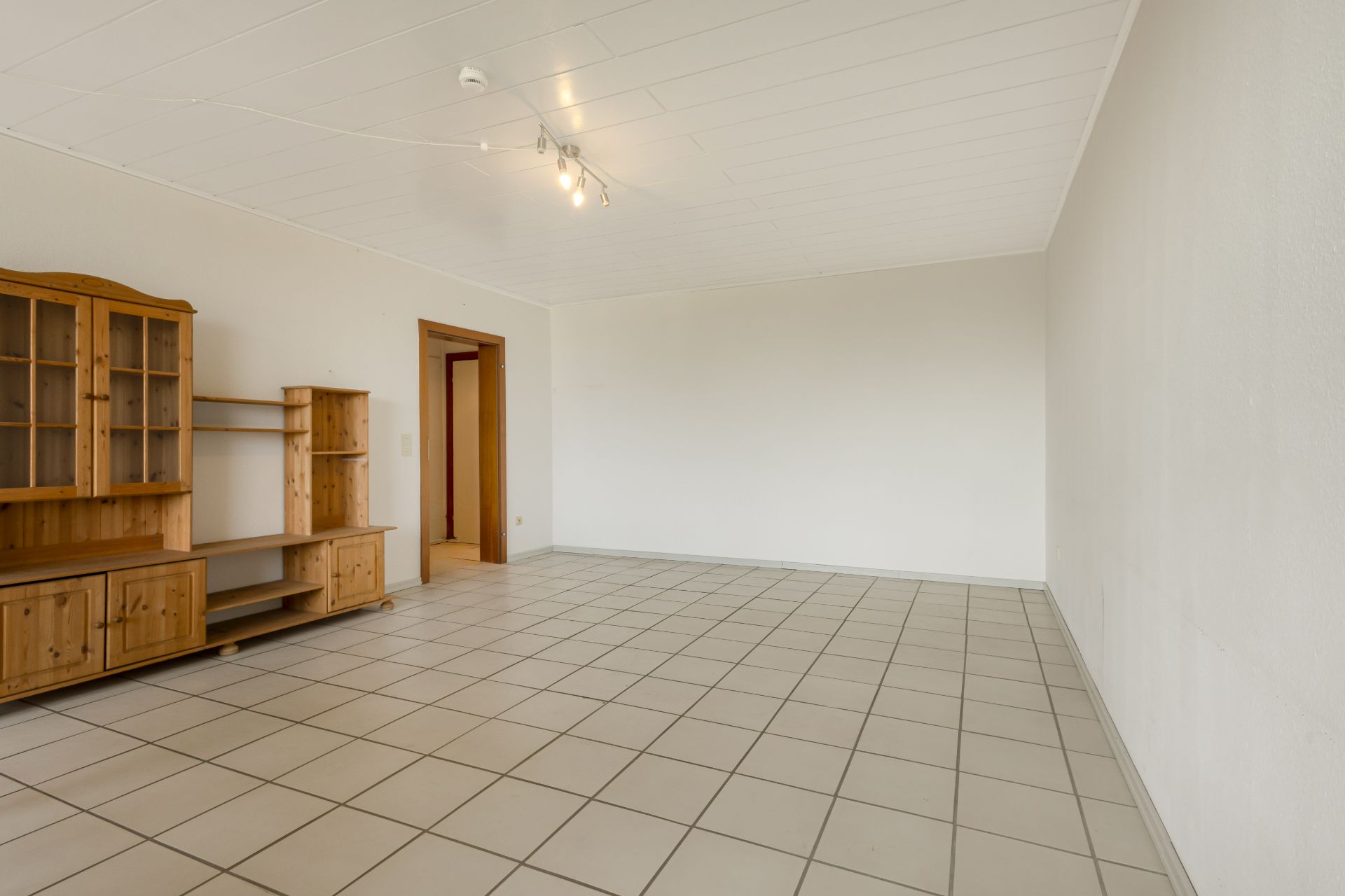 Helles, leeres Zimmer mit Fliesenboden und Holzmöbel an der Wand.