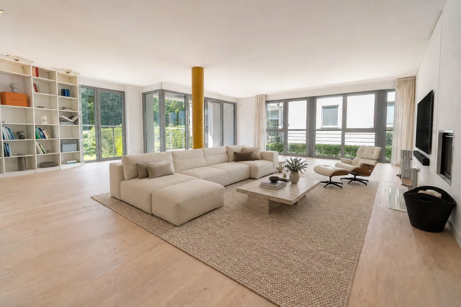 Großes, helles Wohnzimmer mit Sofa, Teppich, Couchtisch, Regal und bodentiefen Fenstern.