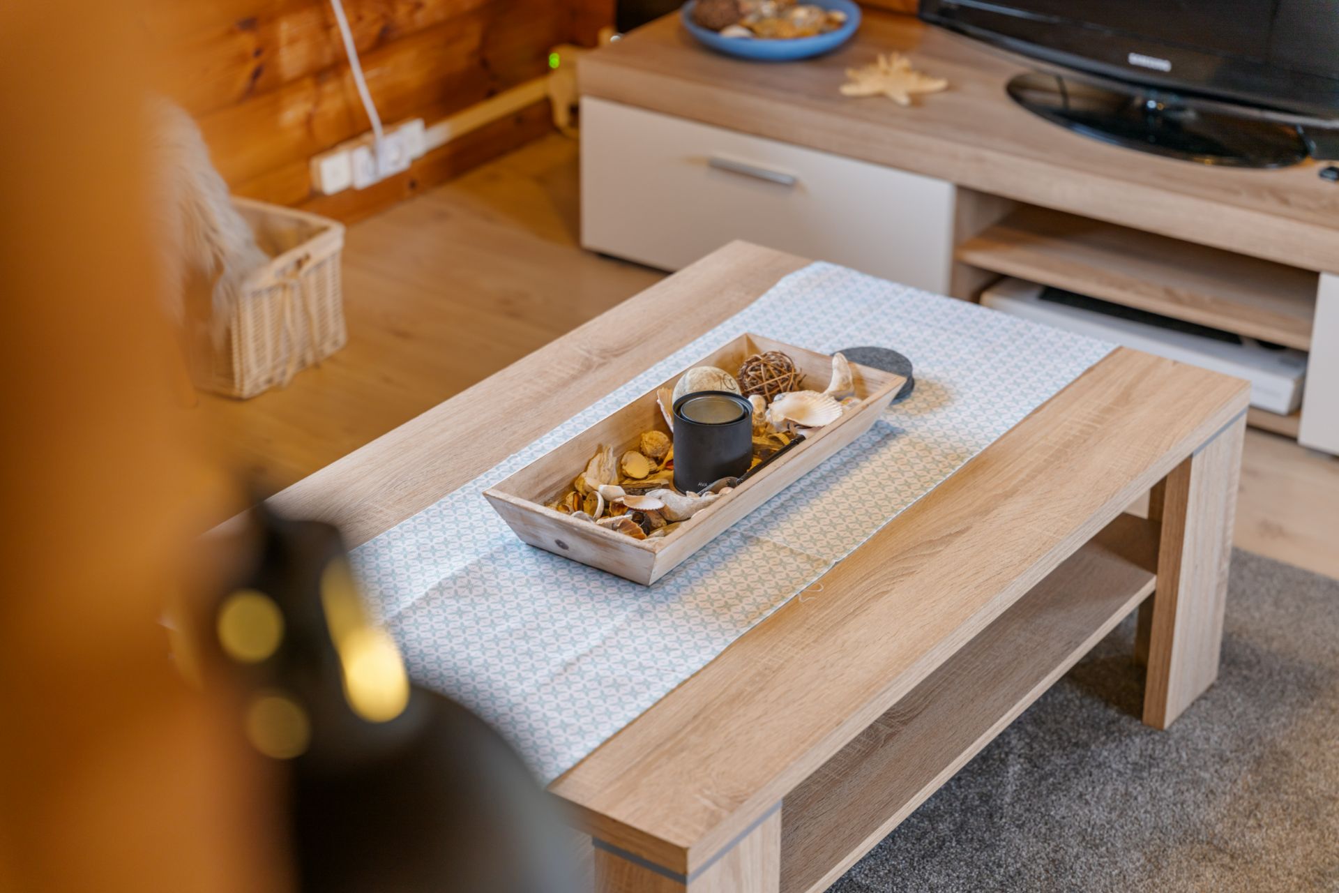 Holztisch mit Dekoschale und Kerze im Wohnzimmer, TV-Möbel im Hintergrund.