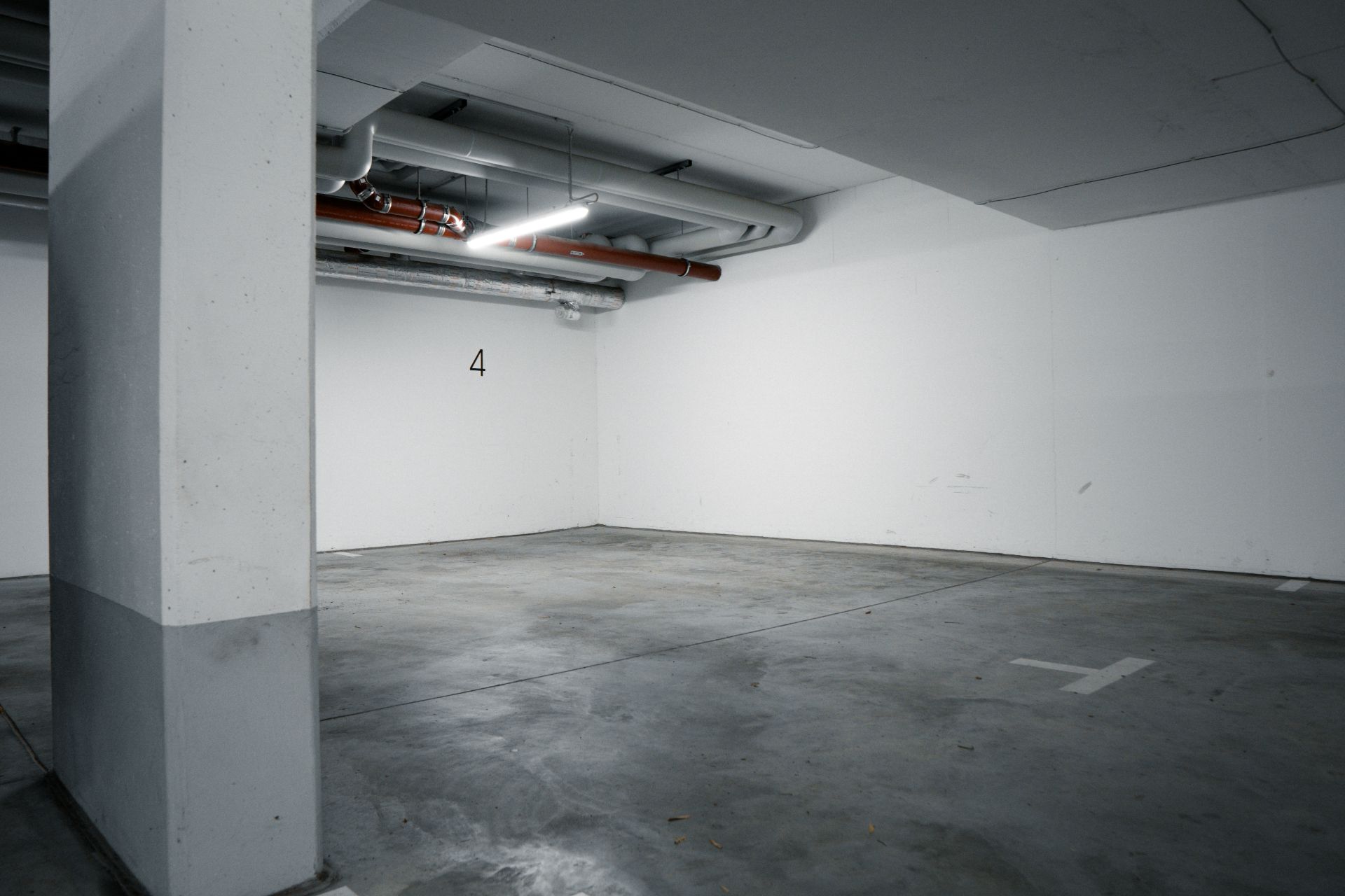 Leerer, beleuchteter Tiefgaragenstellplatz mit der Nummer 4 an der Wand.
