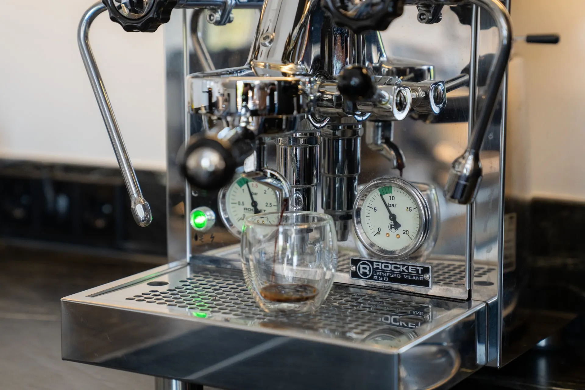 Eine silberne Espressomaschine mit Glas und Manometern auf einer Küchenarbeitsplatte.