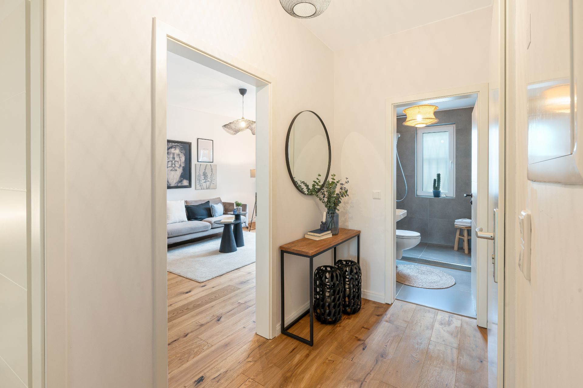 Heller Flur mit Holzboden, Konsole, rundem Spiegel, Blick ins Wohnzimmer und Badezimmer.