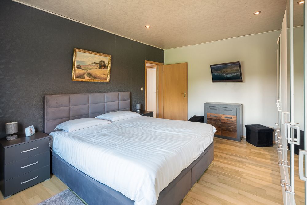 Modernes Schlafzimmer mit Doppelbett, zwei Nachttischen, Kommode und Wandbild.