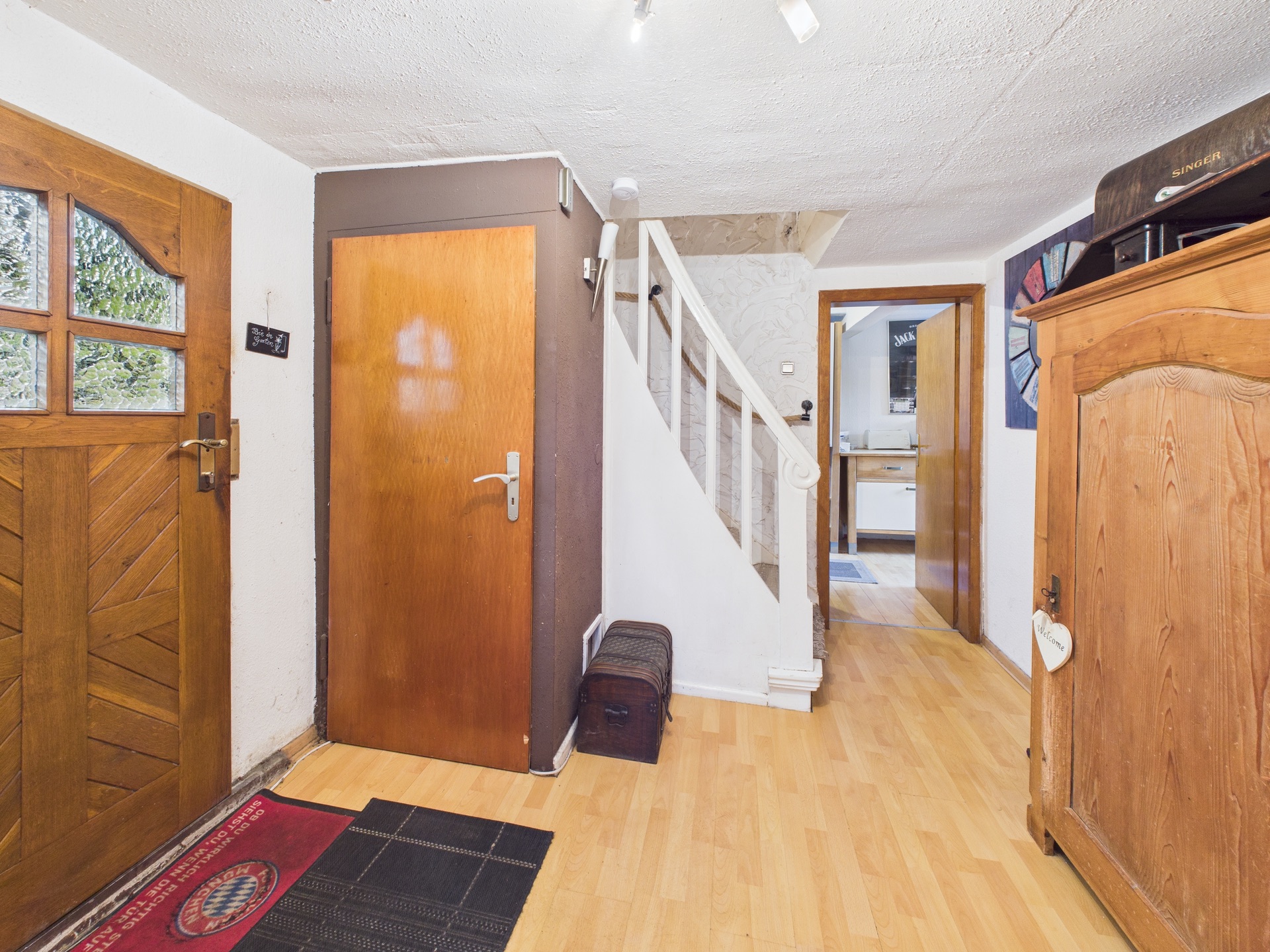Flur mit Holztür, Treppe, Schrank und Parkettboden in einem Wohnhaus.