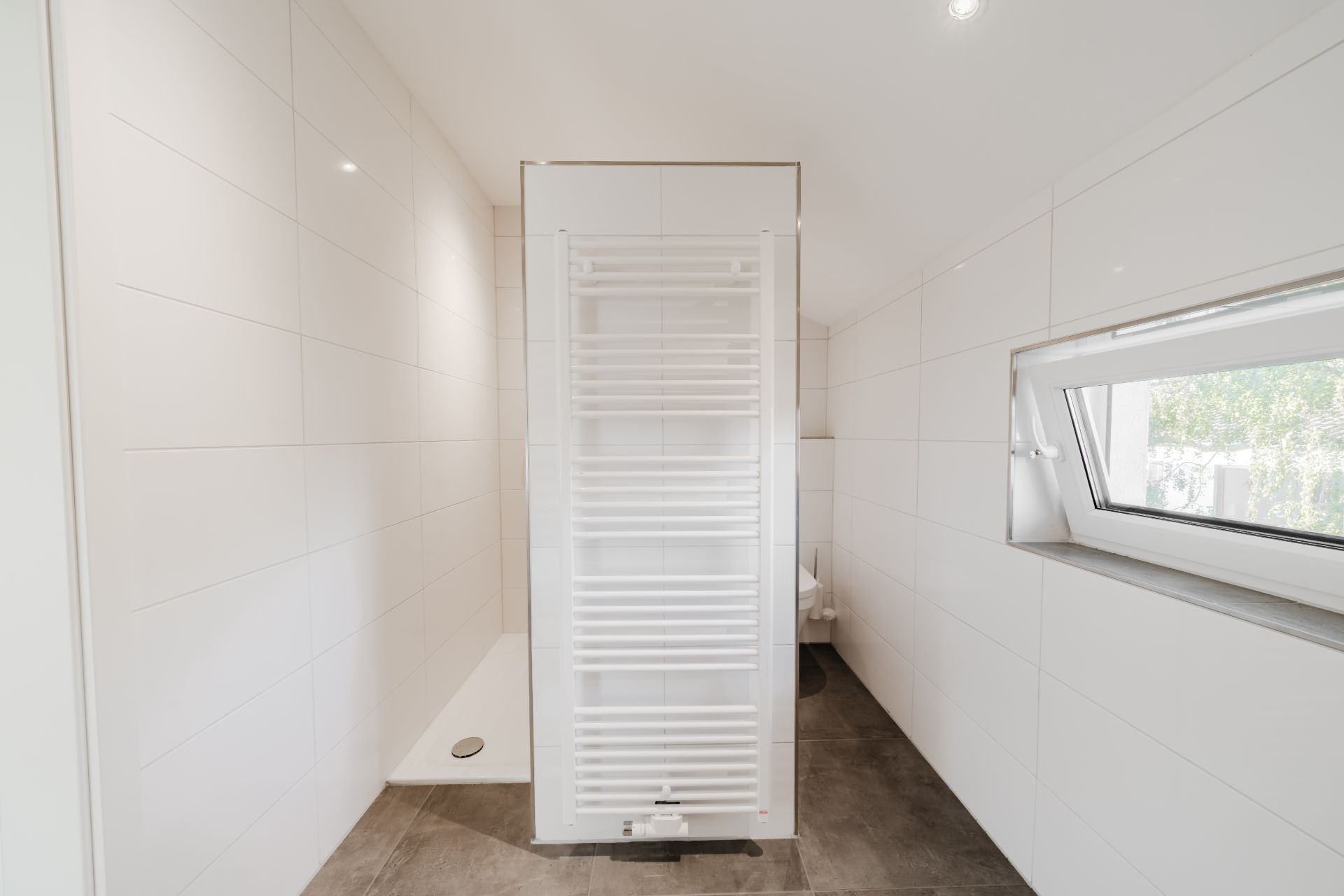 Modernes Badezimmer mit weißem Handtuchheizkörper, Dusche und Fenster.