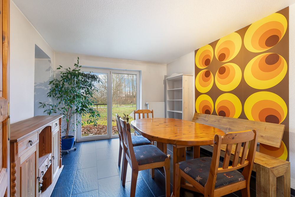 Esszimmer mit Holztisch, Stühlen, bunter Retro-Wand und großer Glastür zum Garten.