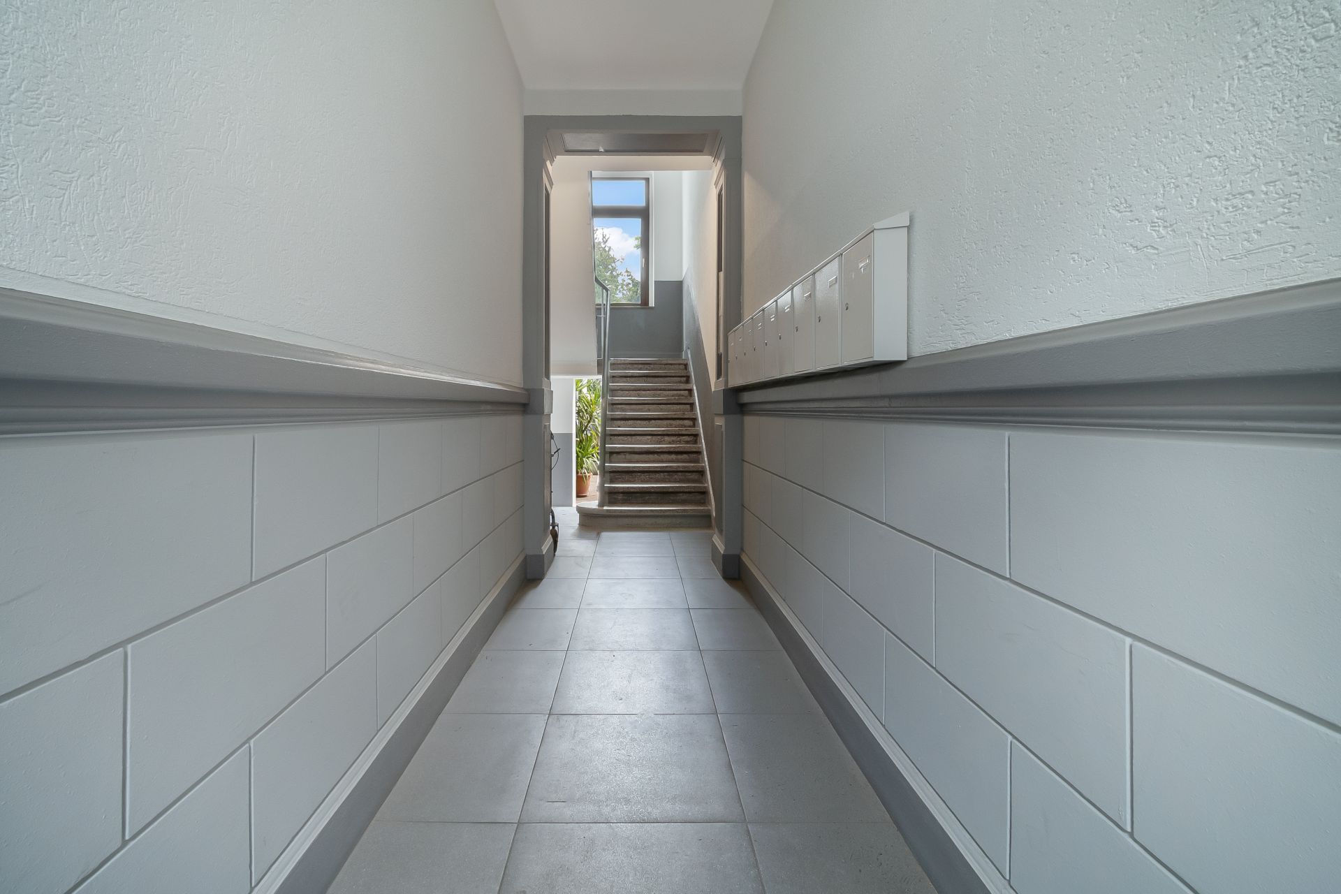Heller Flur mit Briefkästen und Treppe am Ende im Wohnhaus.