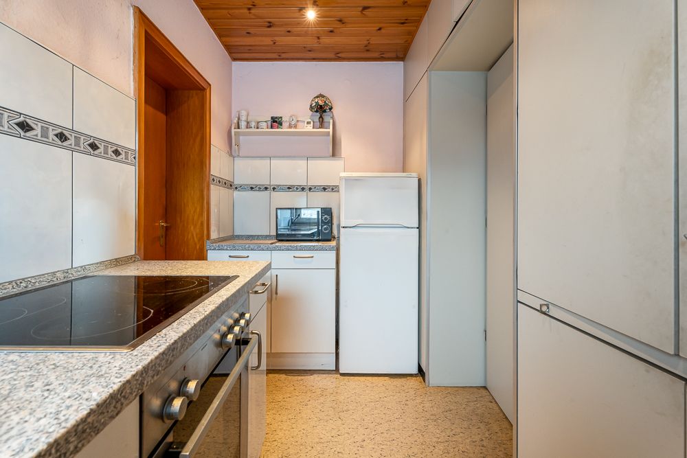 Kleine Küche mit Herd, Kühlschrank, Mikrowelle und weißen Schränken.