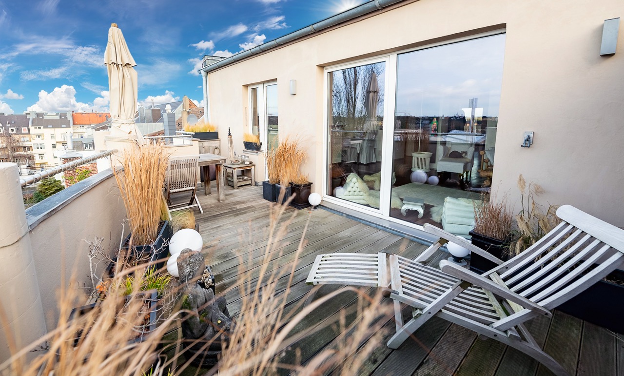 Große Dachterrasse mit Holzliegen, Tisch, Stühlen, Pflanzen und Blick auf die Stadt.