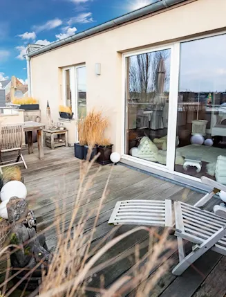 Große Dachterrasse mit Holzliegen, Tisch, Stühlen, Pflanzen und Blick auf die Stadt.