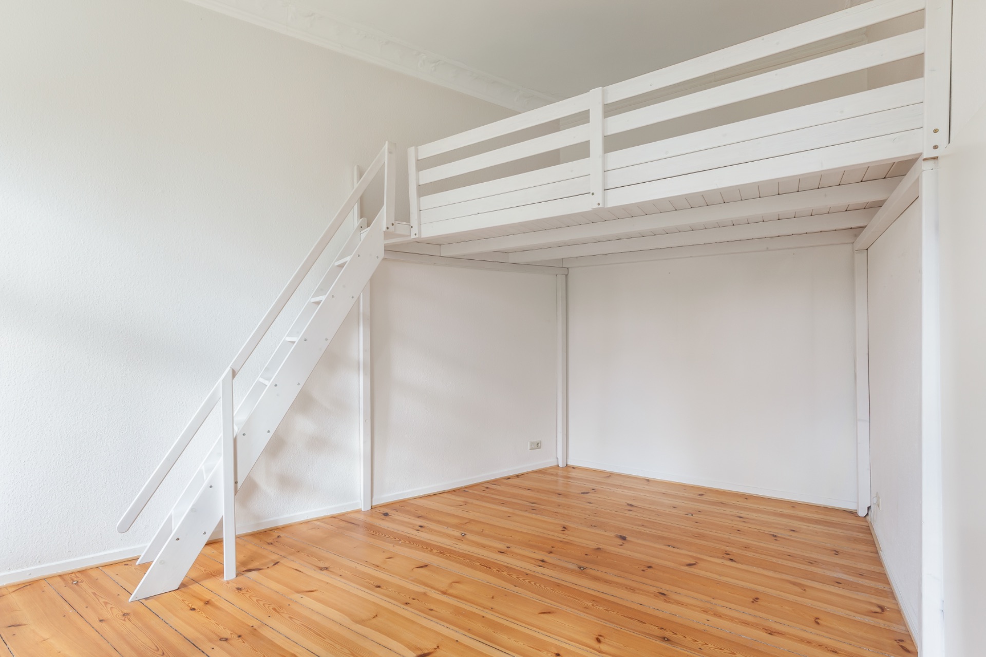Zimmer mit Hochbett aus Holz, weiß gestrichen, und einer Holztreppe, Holzboden.