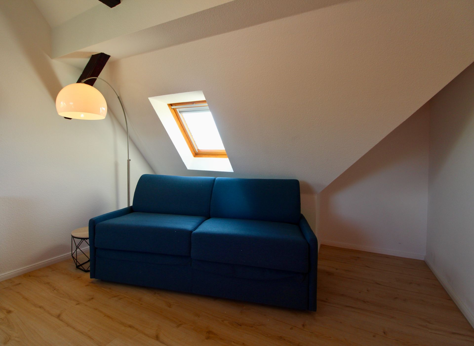 Dunkelblaues Sofa unter Dachschräge mit Stehlampe und kleinem Beistelltisch auf Holzfußboden.