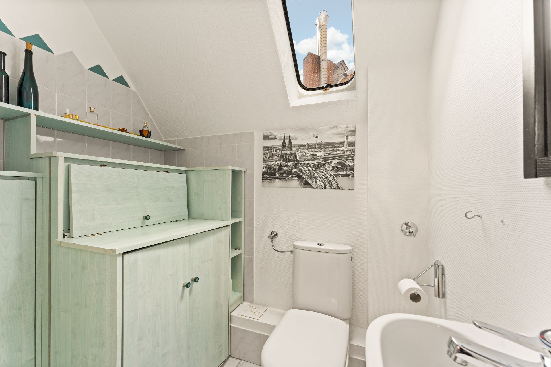 Helles Badezimmer mit Toilette, Waschbecken, Holzschränken und Dachfenster.