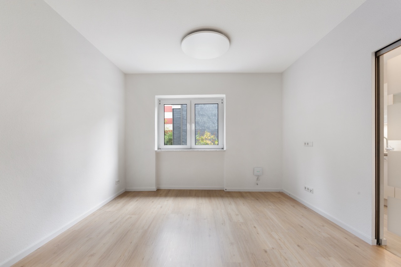 Heller, leerer Raum mit Holzfußboden, weißem Fenster und Deckenleuchte.