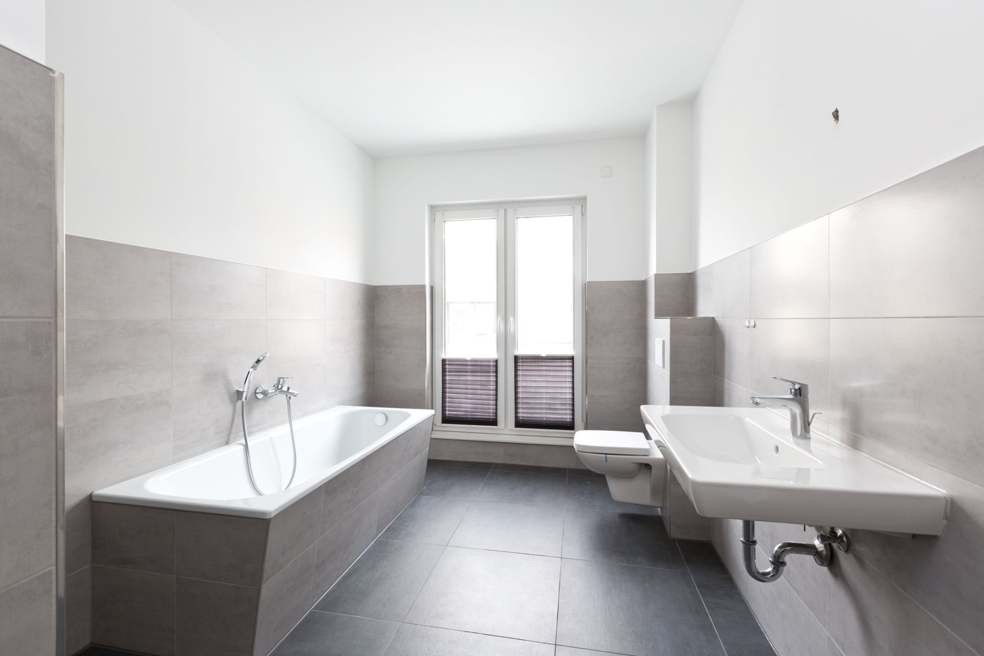 Helles Badezimmer mit Badewanne, Wandwaschbecken, Toilette und Fenster.
