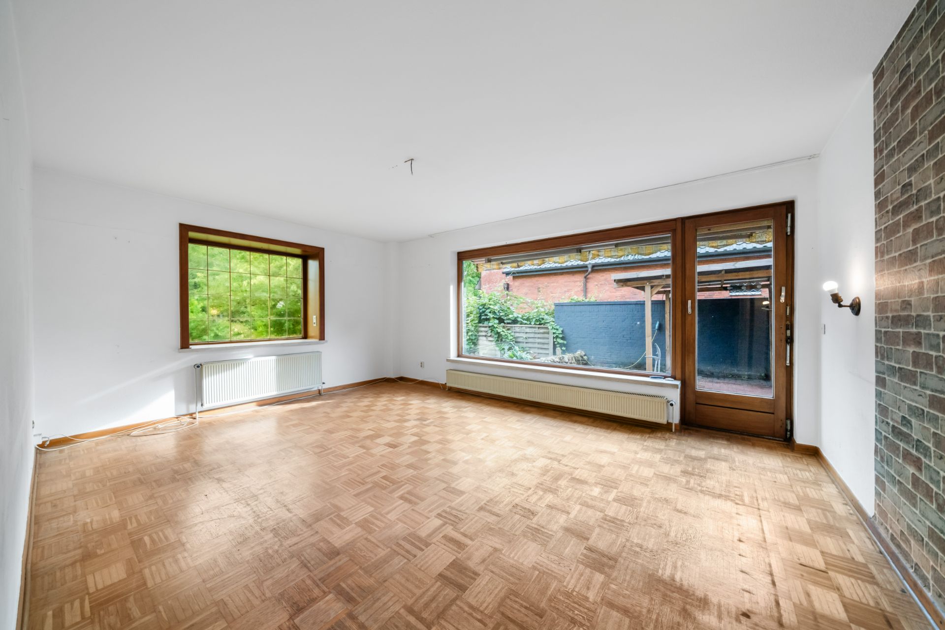 Helles Wohnzimmer mit Parkettboden, großen Fenstern und Tür zum Garten.