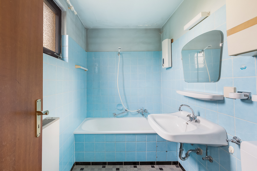 Kleines Badezimmer mit Badewanne, Waschbecken, Spiegel und blauen Fliesen.